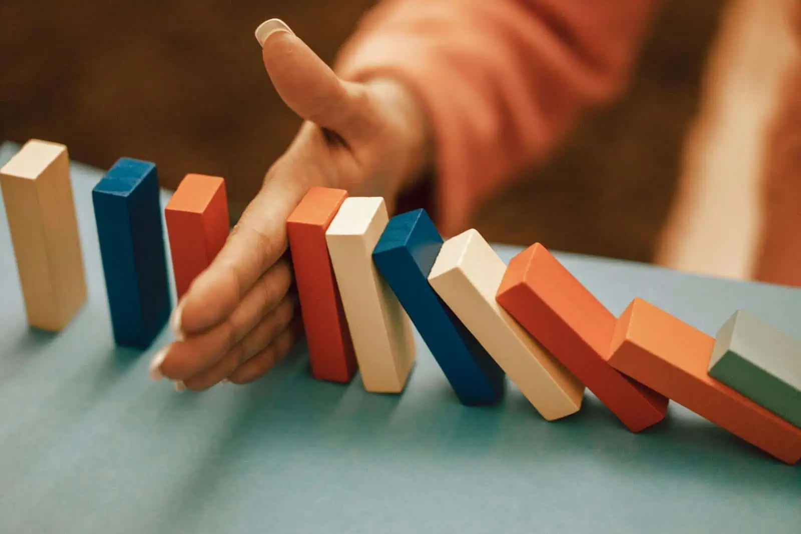 A hand strategically stops falling blue and red domino blocks on a table.